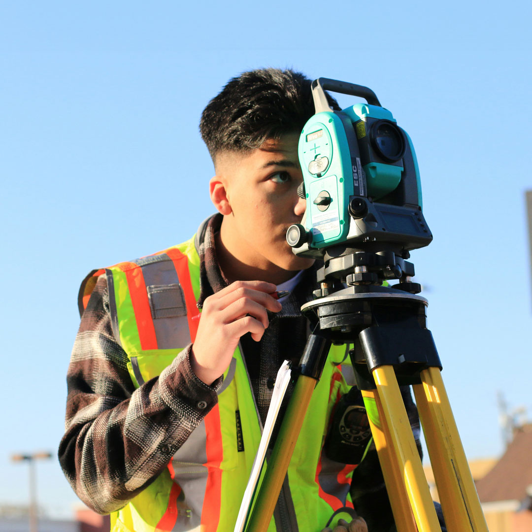 An Indigenous man wearing a safety vest working with surveying equipment