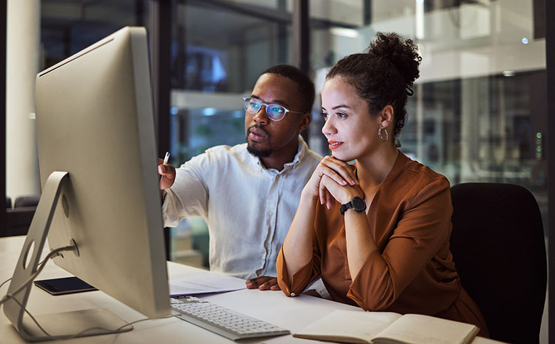 A male and female co-worker reviewing infomration on a computer screen together