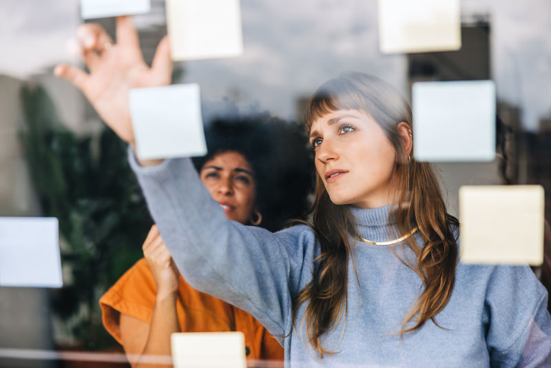 Two female co-workers looking at post-it notes stuck to a window