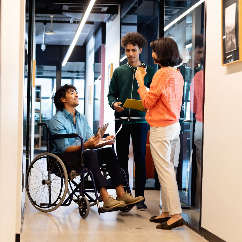 A group of three colleagues having a conversion in a hallway. One is in a wheelchair