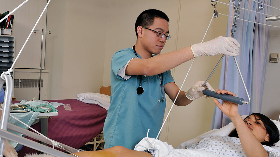 A male nurse assisting a patient laying in bed