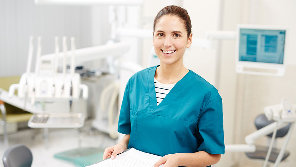 A smiling women working in a dentist office wearing scrubs