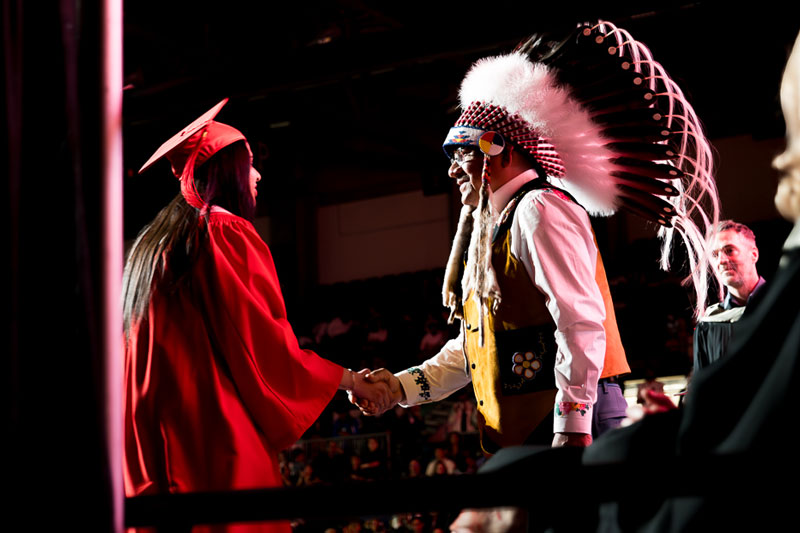 Indigenous man shaking hand with female student in red robe