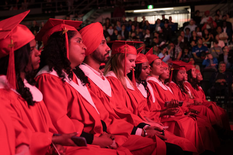 Students in red robes sitting facing stage