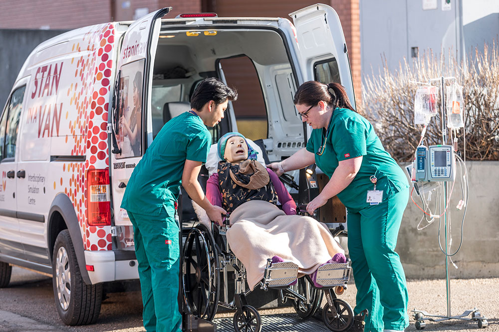 Two nursing students loading a simulation dummy into the back of a van.