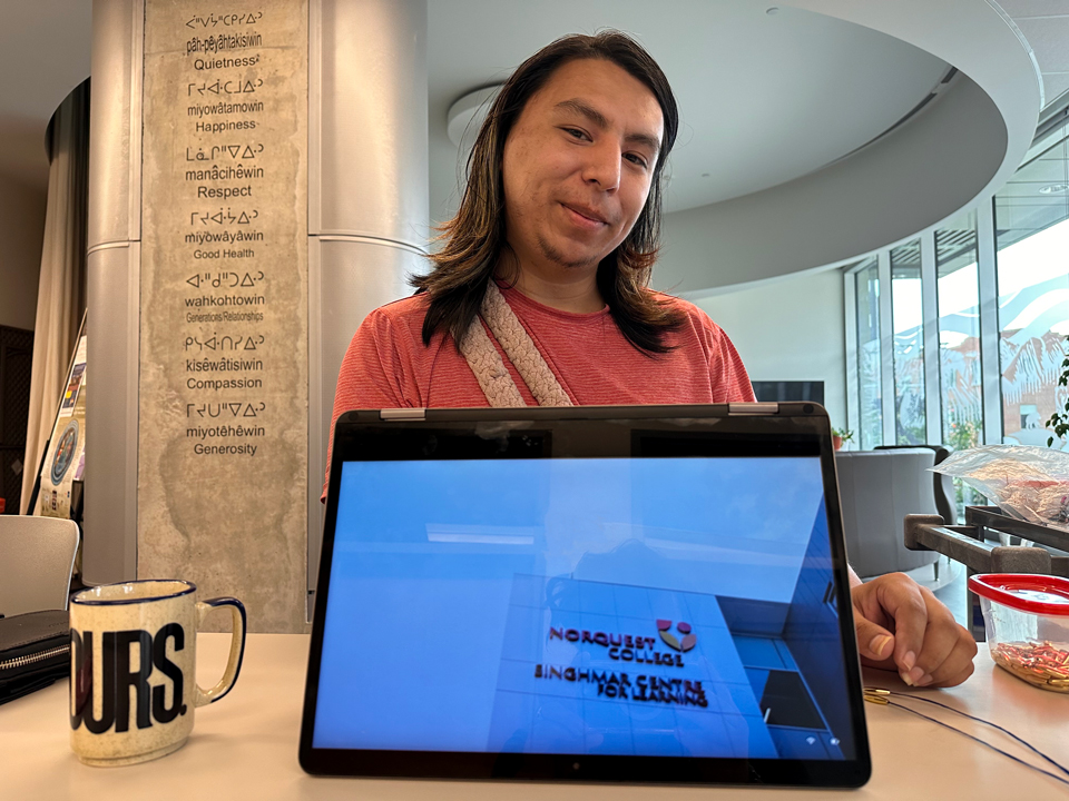 An smiling Indigenous man standing in front of a computer in Indigenous student centre