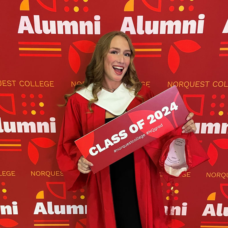 Anna wearing a red graduation robe holding a sign that reads class of 2024